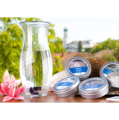 Wasserglas mit Blumen und Duftkerzen in Dosen auf einem Tisch im Freien.