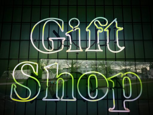 Leuchtender Schriftzug "Gift Shop" auf einer reflektierenden Fensterscheibe.